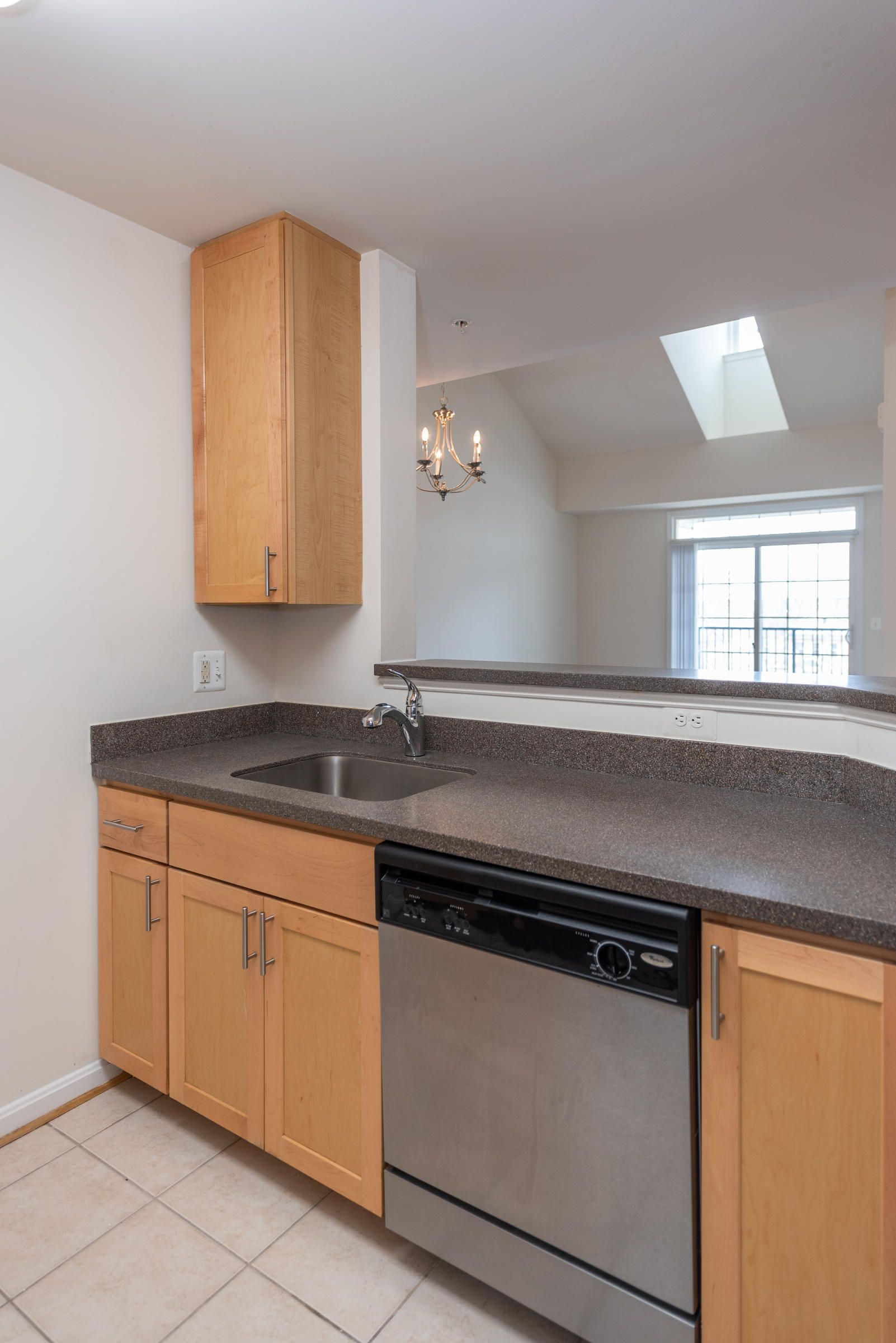 Modern kitchen with light wood cabinets, a stainless steel dishwasher, sink, and a granite countertop.