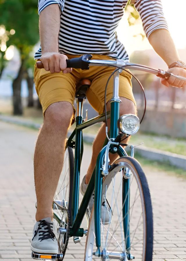 Person in a striped shirt and yellow shorts riding a bike on a sunlit park path.
