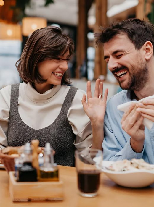 A smiling couple sits at a restaurant table, laughing and enjoying their meal together.